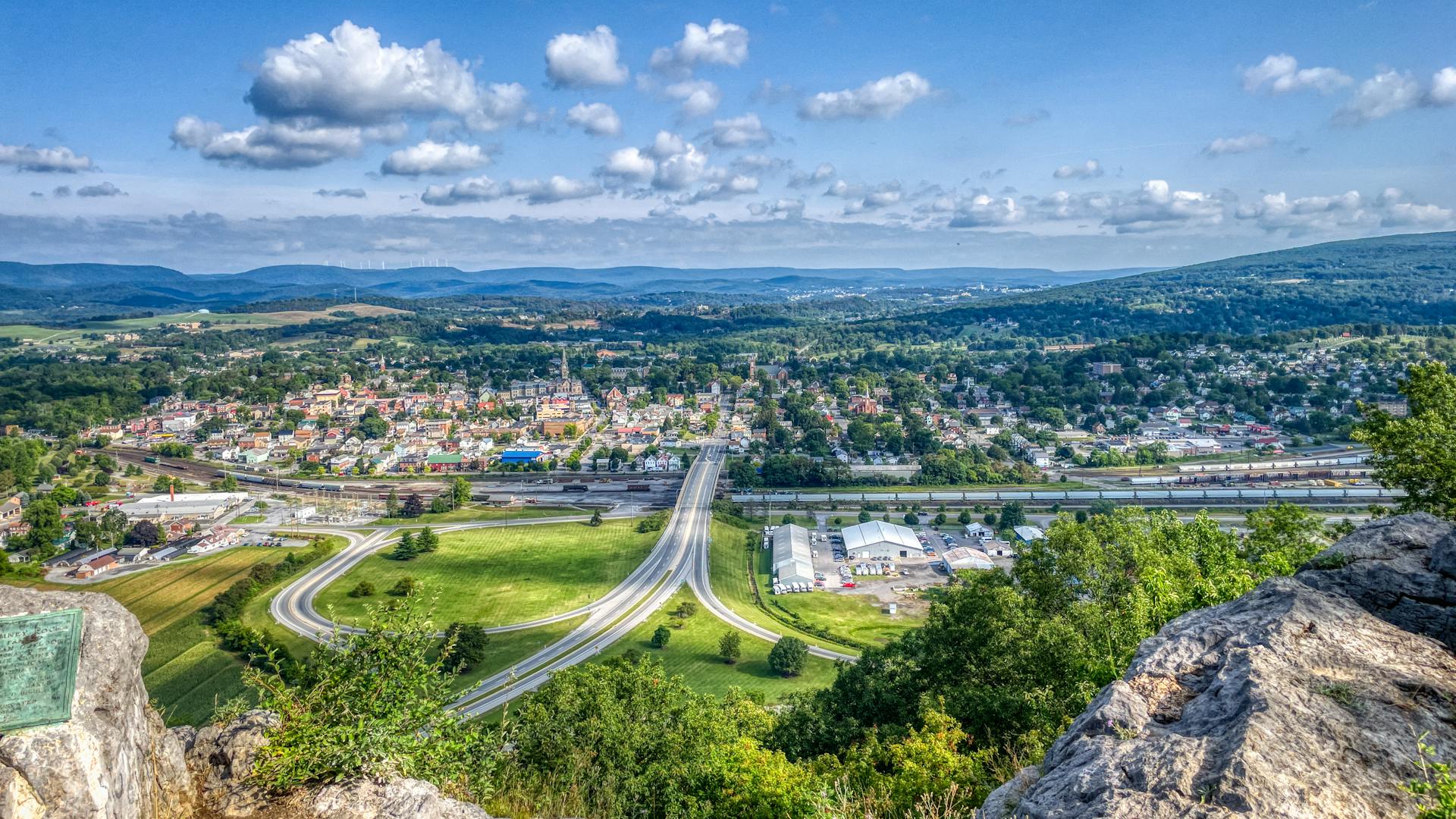 A breathtaking aerial view of Hollidaysburg, PA with rolling hills, roads, and clear blue sky.