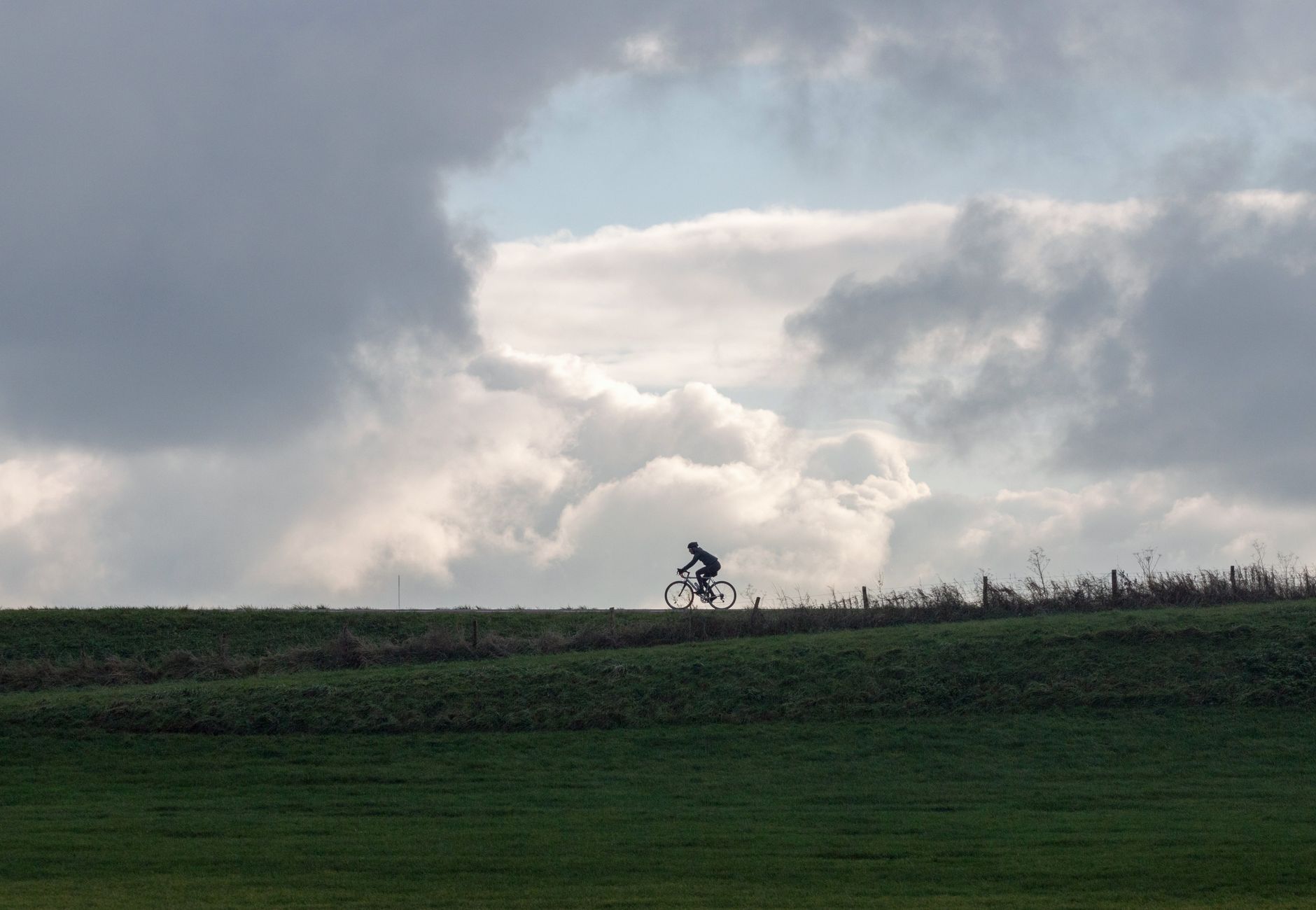 Cyclist riding on a hill in Nederland with clouds overhead, creating a dramatic silhouette effect.