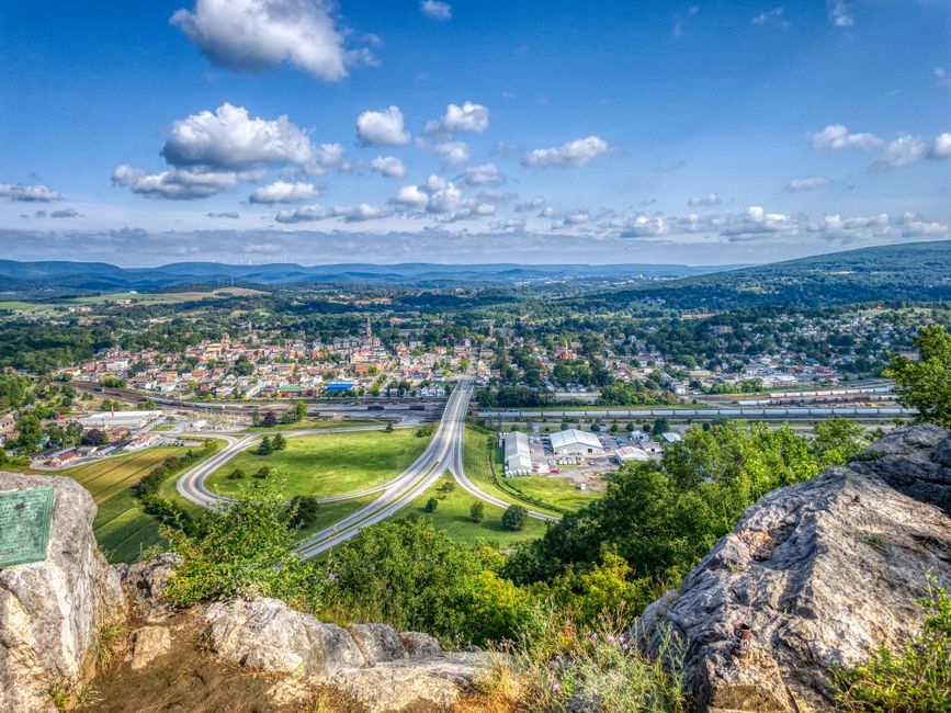 A breathtaking aerial view of Hollidaysburg, PA with rolling hills, roads, and clear blue sky.