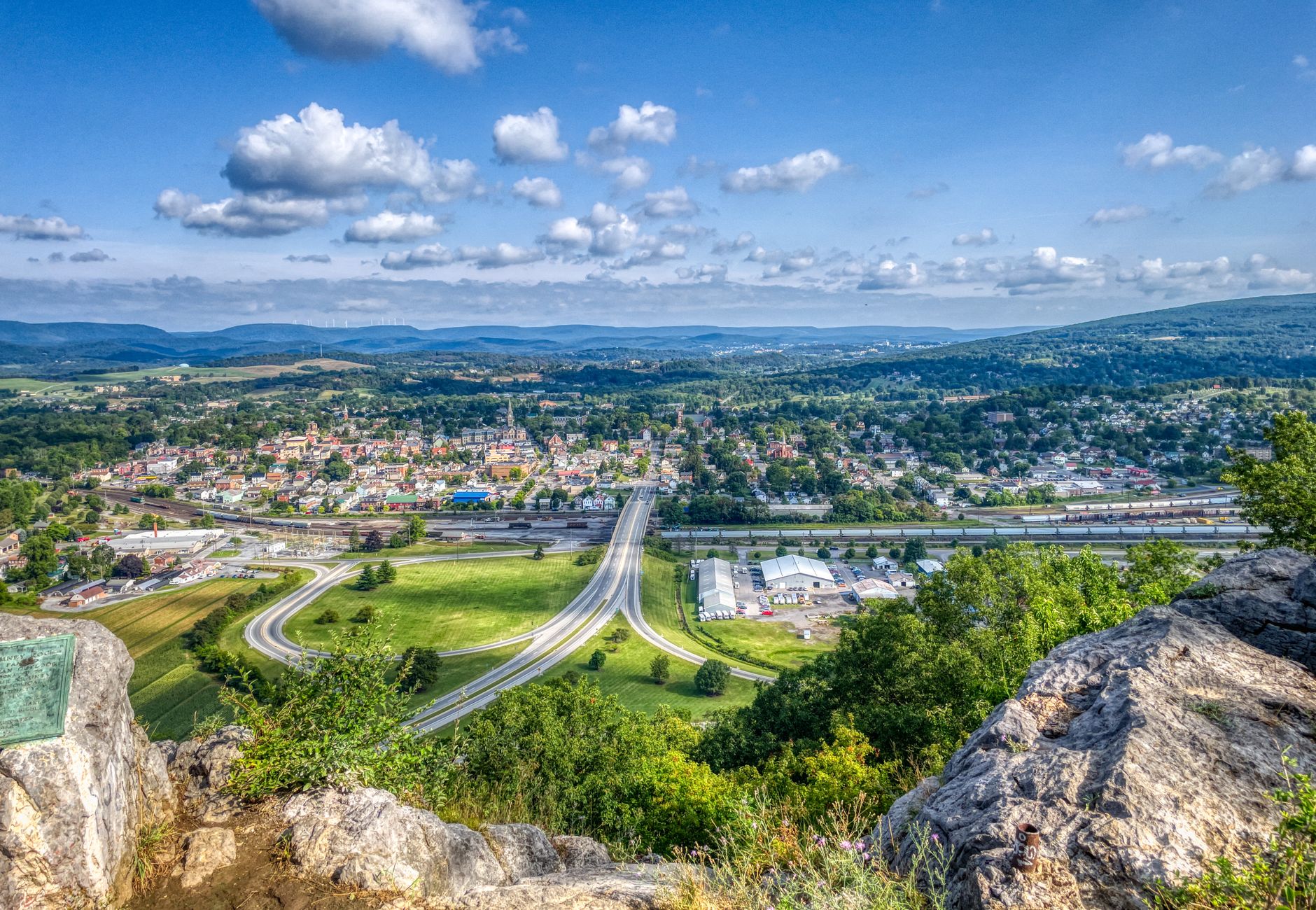 A breathtaking aerial view of Hollidaysburg, PA with rolling hills, roads, and clear blue sky.